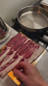 Julia lifts a slice of bacon from the beautifully presented Pheasants' Hill Farm packaging and places on a stainless steel frying pan, ready to cook. The  packaging is an eco-made vacuum-packed pouch, with bacon rashers displayed neatly in a row on a bacon board. 
